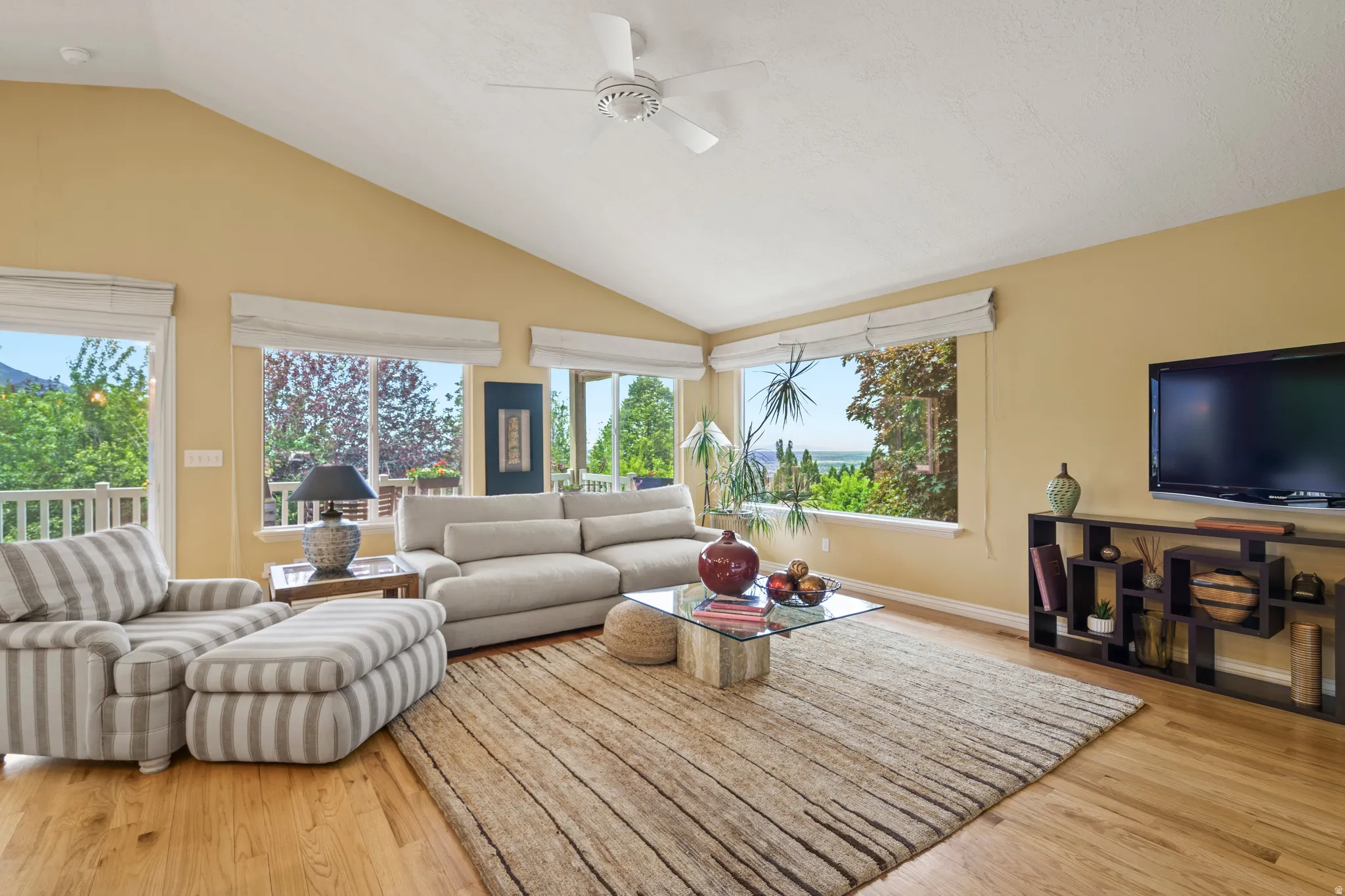 Living space featuring vaulted ceilings, big windows beautiful view natural light coming through,  wood-finish flooring, a ceiling fan.