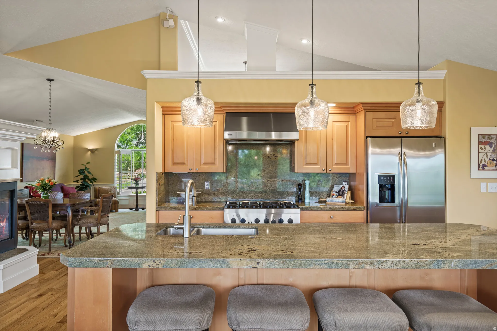 Kitchen featuring a large natural stone island with seating, stainless steel appliances, wood cabinetry, and pendant lighting