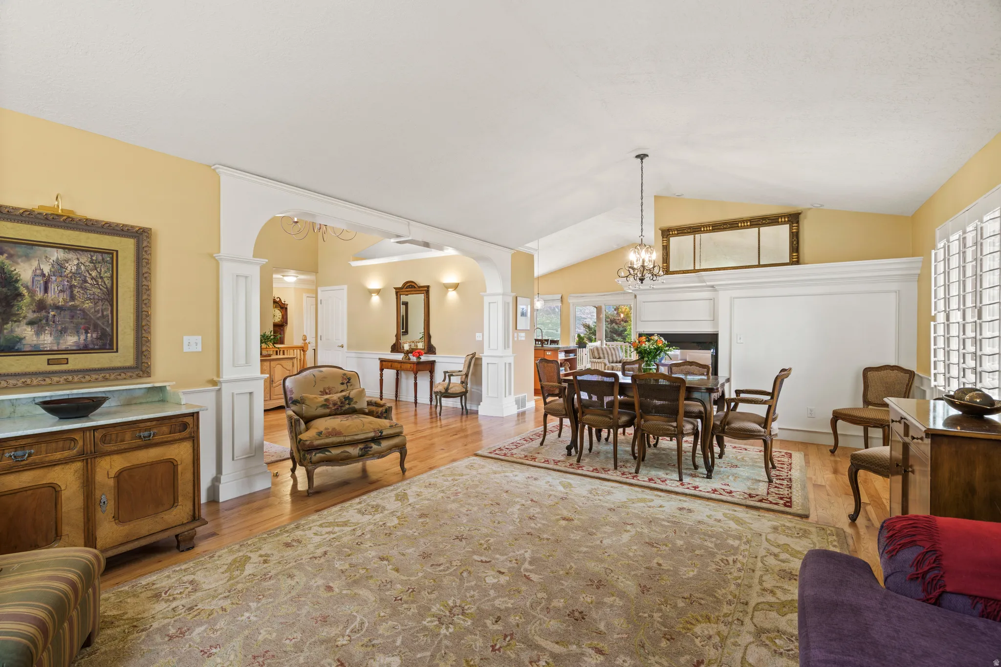 Vaulted ceiling, facing the formal  dining area featuring a fireplace, chandelier, wood-finish flooring, and arched entryway with decorative trim