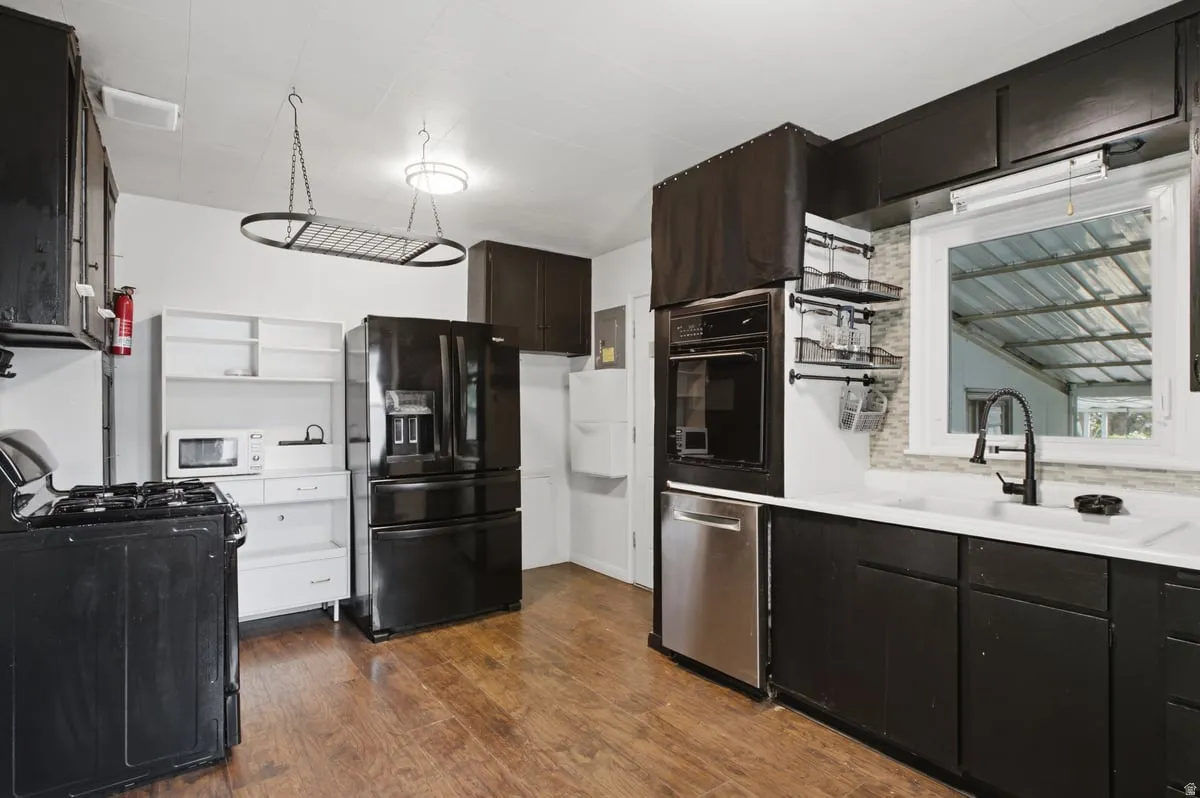 Wood-finish flooring with black cabinetry, stainless steel dishwasher, and an built oven