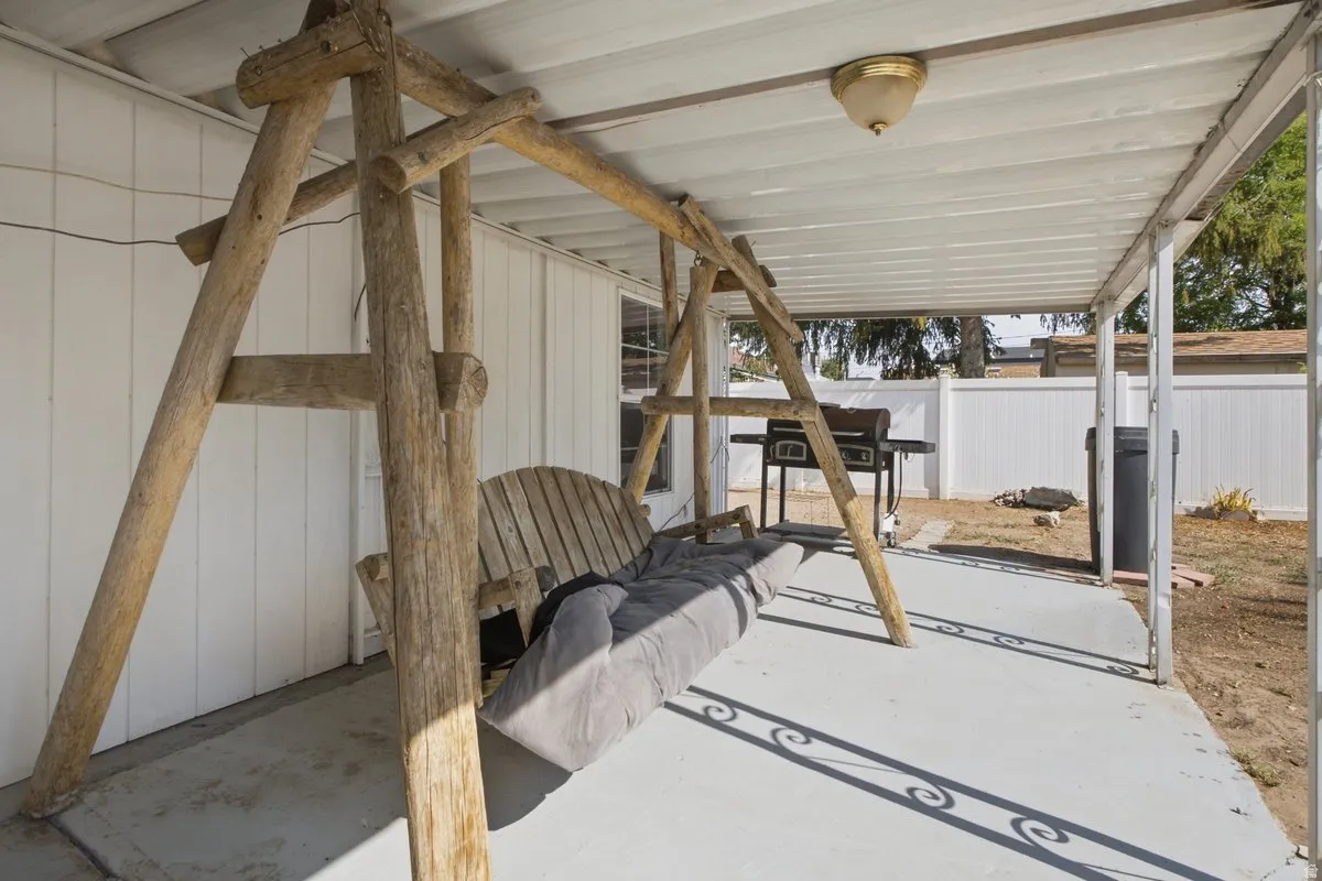 Covered patio with a mounted light fixture, concrete flooring, and an enclosed backyard featuring a white privacy fence
