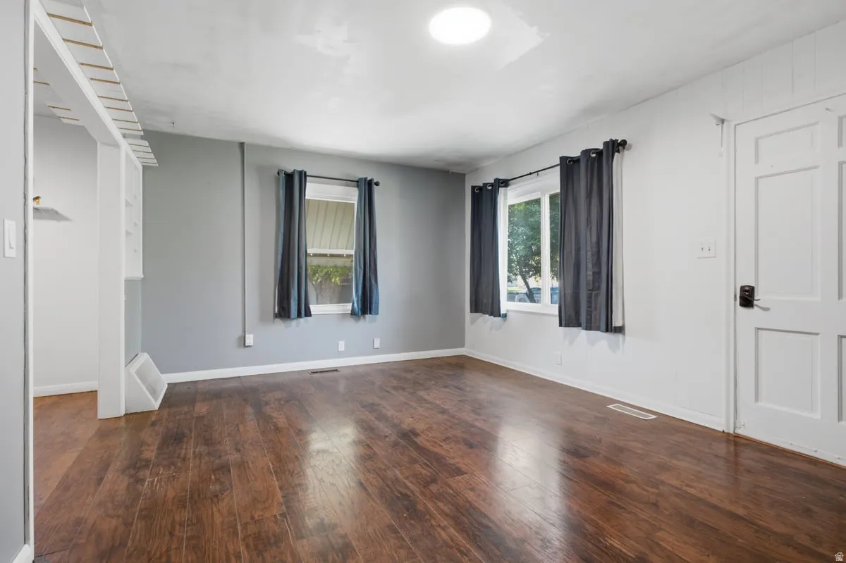 Living Room. Wood-finish flooring throughout, two windows, recessed ceiling light, paneled door, and built-in shelving