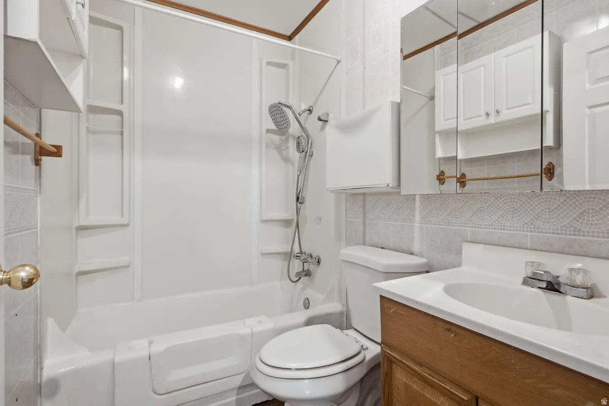 Full bathroom featuring a shower-tub combination, wood-finish vanity with a white basin, mirrored medicine cabinet, and tiled walls