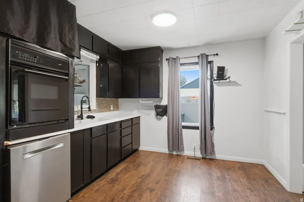 Wood-finish flooring, dark cabinetry, white countertops, built-in oven, and stainless steel dishwasher
