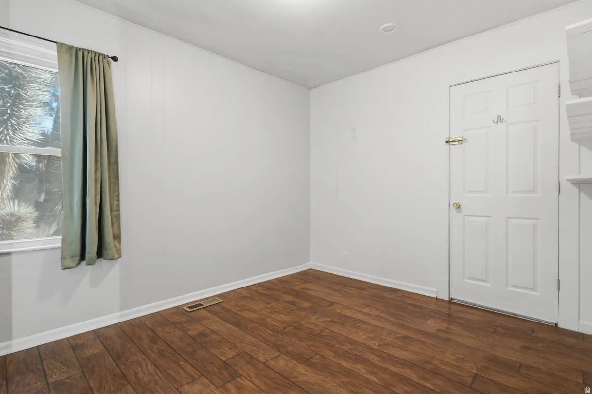 Bedroom #2 that leads to laundry. Wood-finish flooring with white baseboards, a white paneled door, and a single window