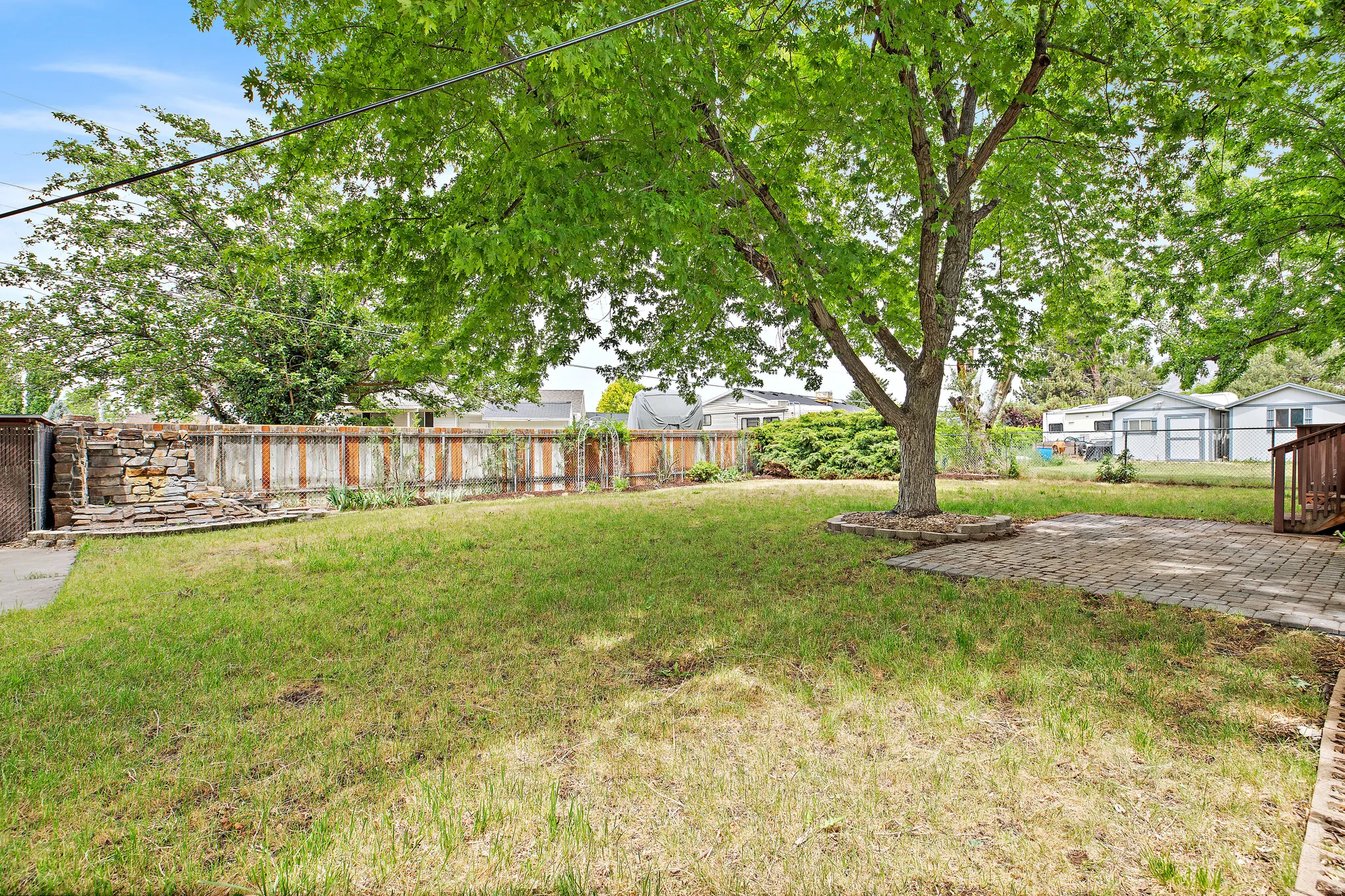 Expansive backyard featuring a mature shade tree, a paver patio, and a wood fence
