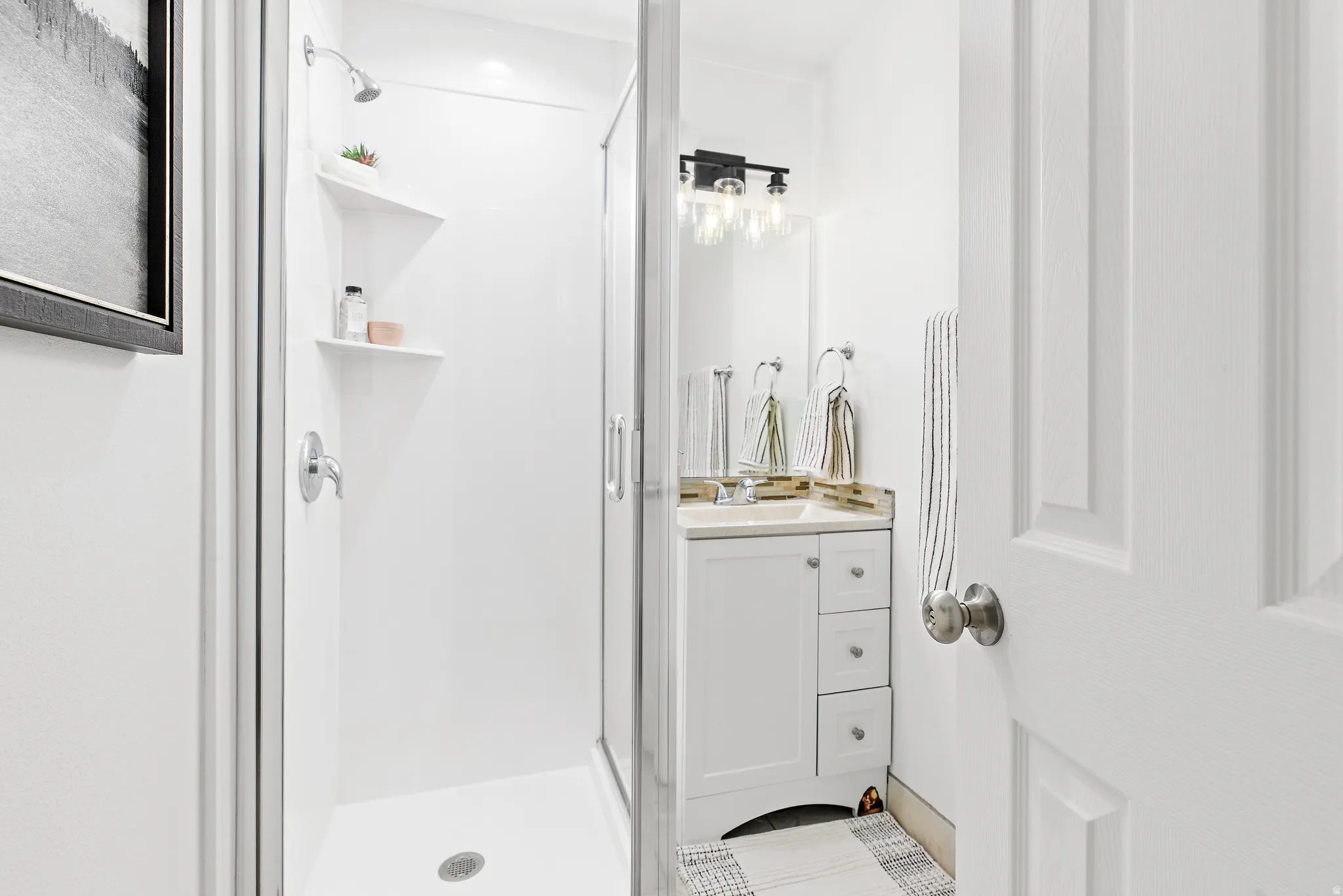 Compact bathroom featuring a shower enclosure with built-in shelving, a single vanity with a light-toned countertop, and modern wall-mounted lighting