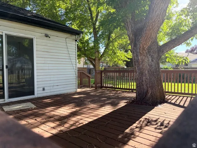 Expansive wooden deck with a built-in railing system, featuring a mature tree, adjacent to horizontal siding and a sliding glass door