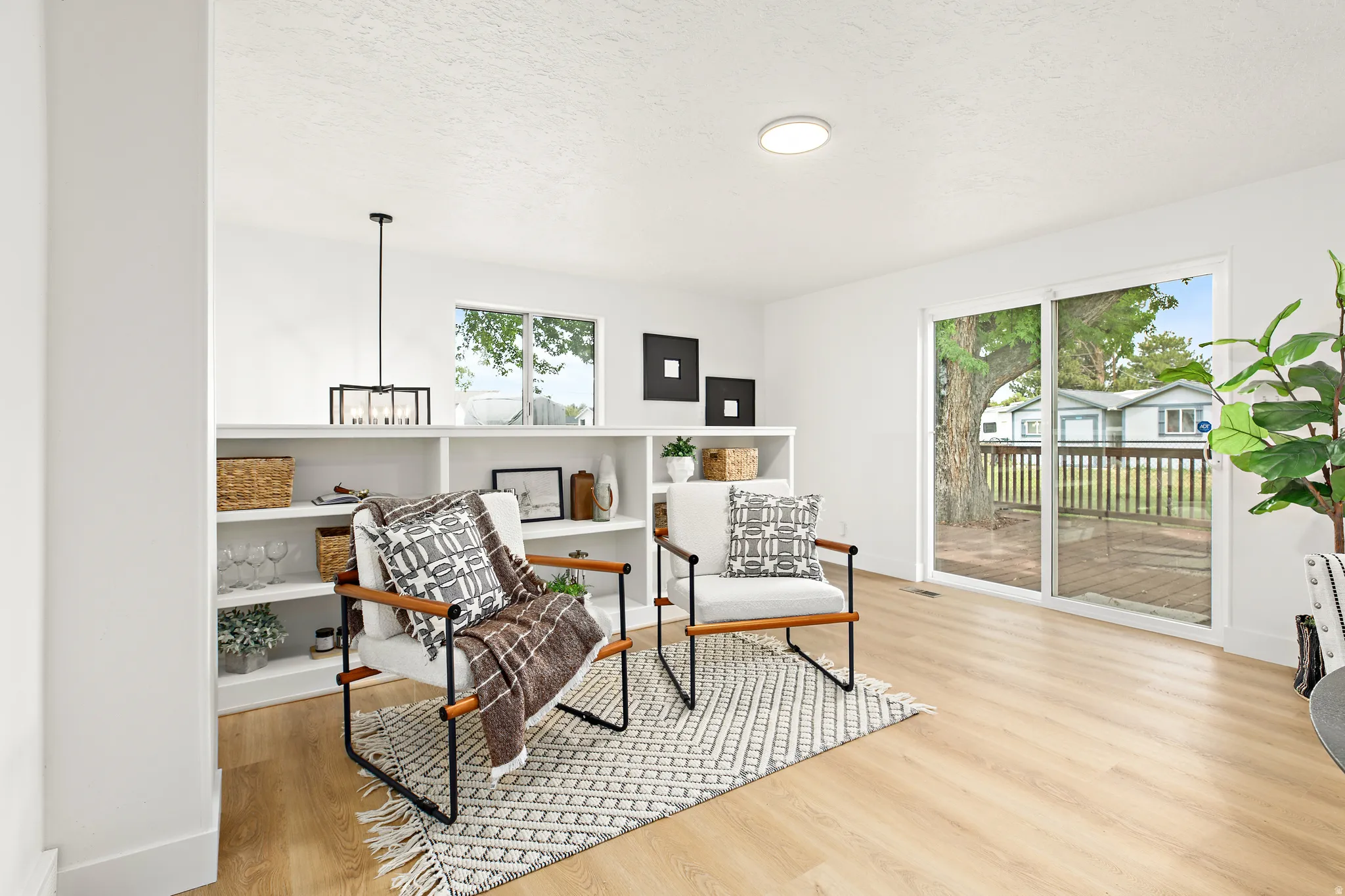 Inviting interior space featuring wood-finish flooring, a full wall of built-in shelving, and white walls. Sliding glass doors let in plenty of light and give easy access to the inviting deck