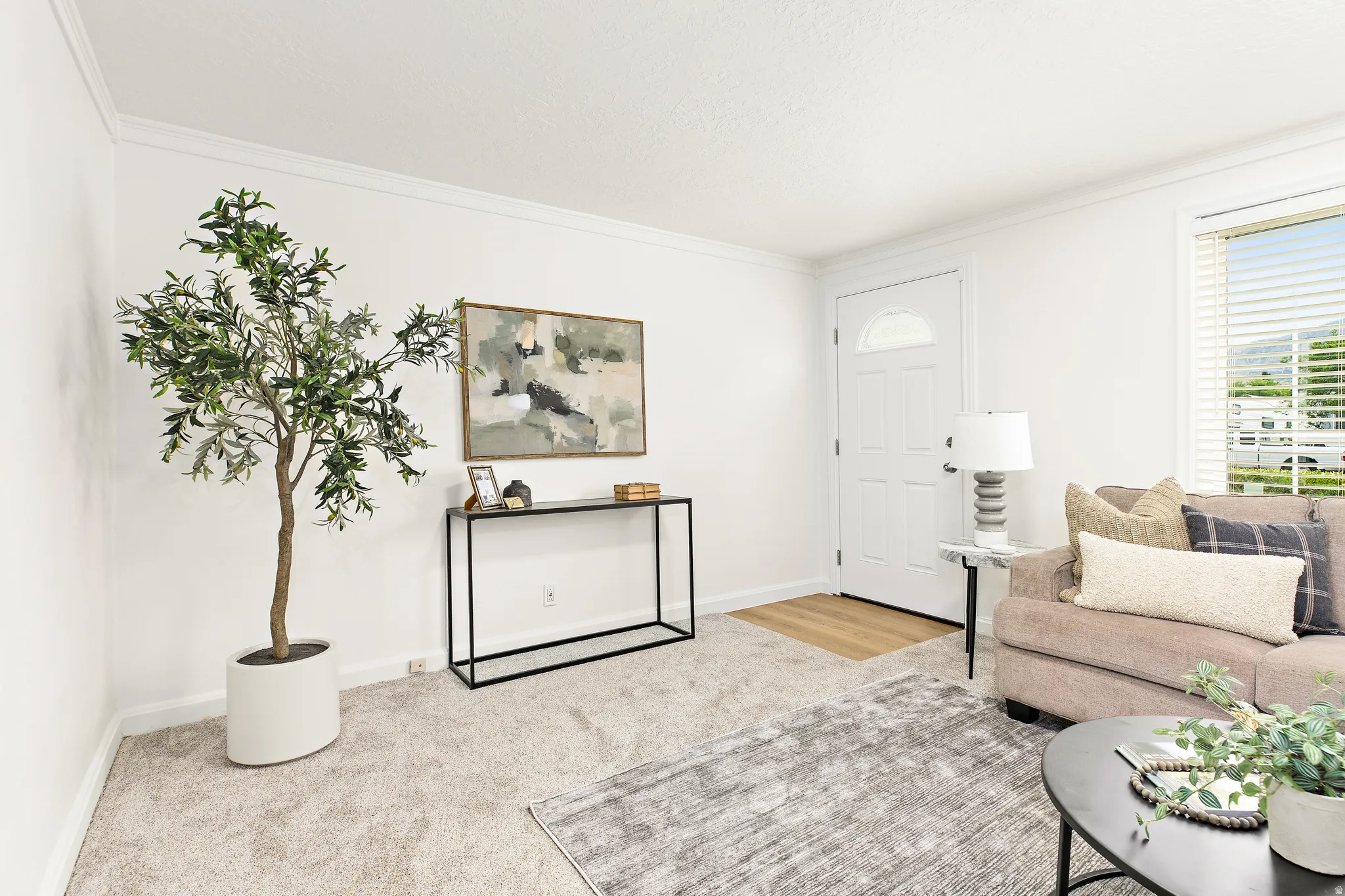 Bright living area featuring a paneled entry door with an arched window, crown molding, and light-toned carpeting