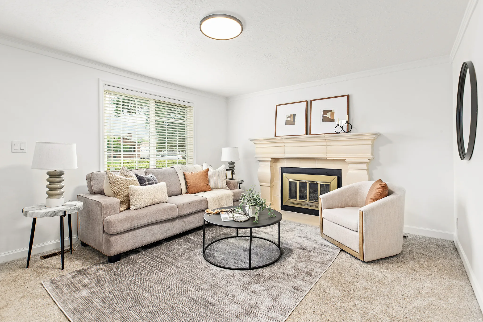 Living area featuring a prominent fireplace with a carved mantel, light-toned carpeting, a large window with blinds, and ceiling-mounted lighting