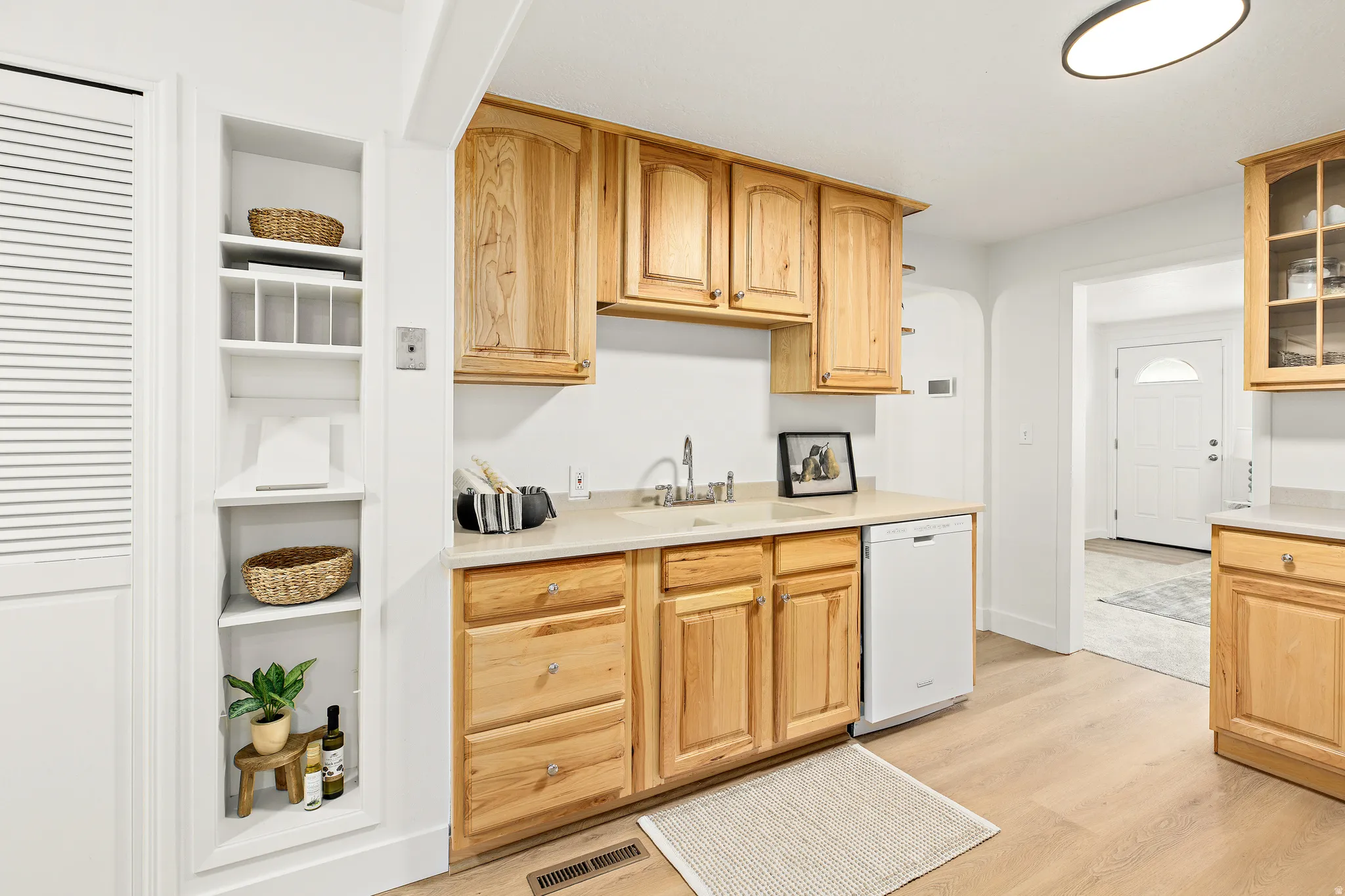 Kitchen area featuring wood cabinetry, light-toned countertops, a stainless steel sink, and a built-in dishwasher