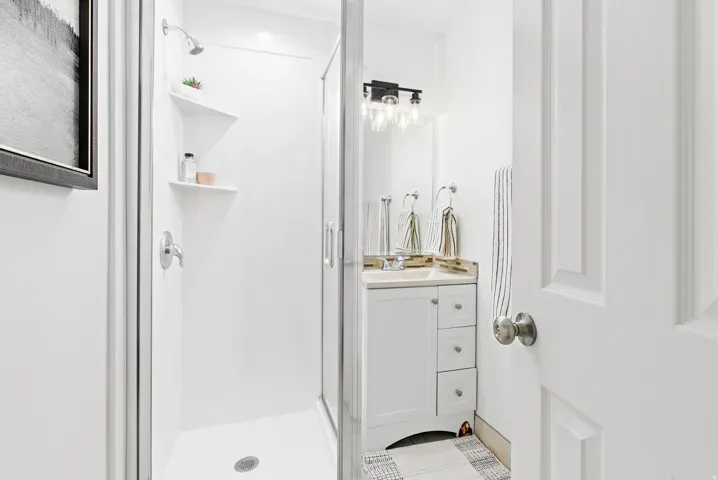 Compact bathroom featuring a shower enclosure with built-in shelving, a single vanity with a light-toned countertop, and modern wall-mounted lighting