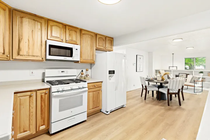 Open-concept kitchen and dining area featuring light-toned wood cabinetry, white appliances, and wood-finish flooring