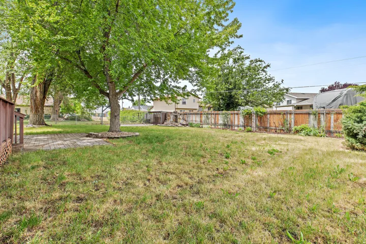 Spacious backyard featuring a brick paver patio, established trees, basketball hoop, extra storage, fountain, pond, and a wood privacy fence