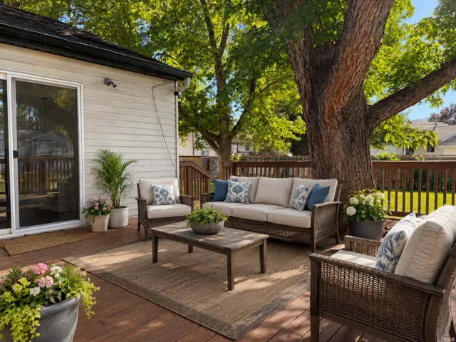 Spacious wood-finish deck with perimeter fencing, mature trees, and sliding glass door access to the residence