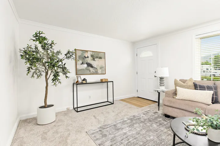 Bright living area featuring a paneled entry door with an arched window, crown molding, and light-toned carpeting