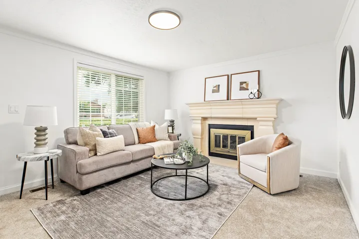 Living area featuring a prominent fireplace with a carved mantel, light-toned carpeting, a large window with blinds, and ceiling-mounted lighting