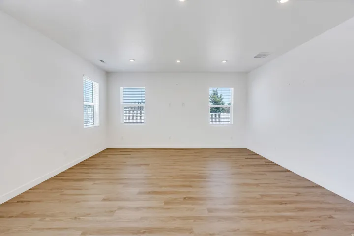 Spacious room featuring wood-finish flooring, white baseboards, and bright white walls