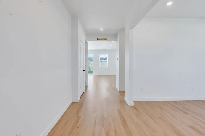 Open-concept interior featuring light wood-finish flooring, recessed lighting, and crisp white walls