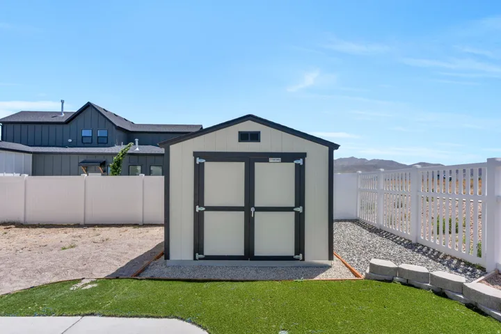Two-tone storage shed with dual barn doors and an overhead vent, situated on a gravel pad