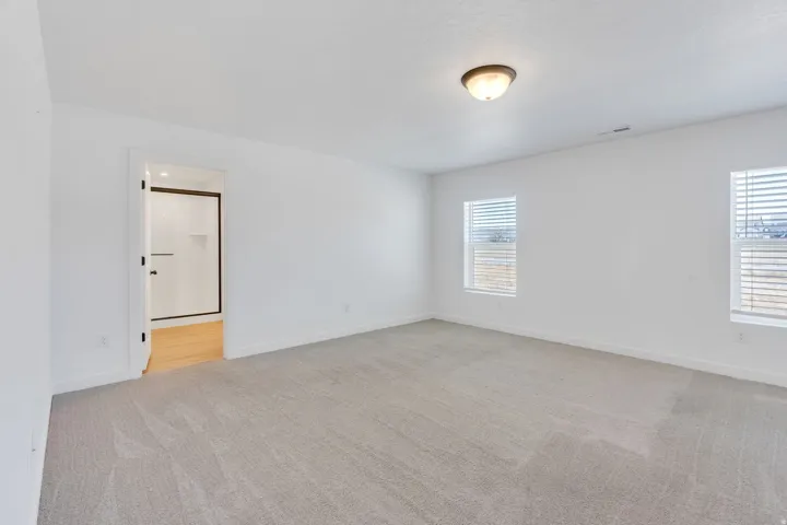 Spacious room featuring neutral carpet flooring, white walls, and two windows with horizontal blinds