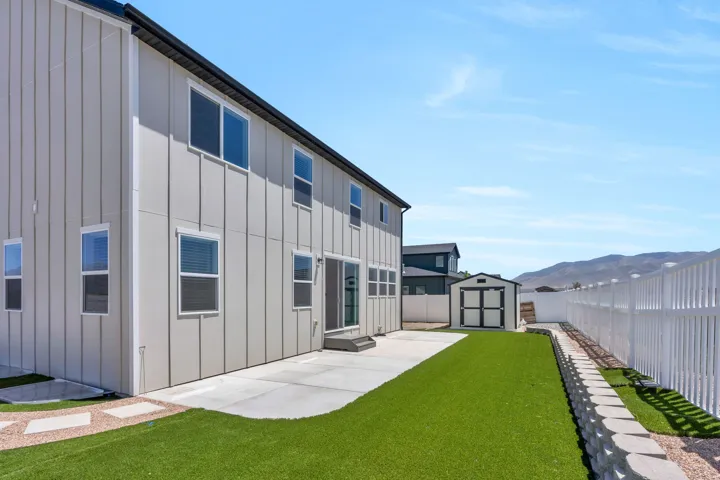 Expansive rear patio area featuring a concrete pad, artificial turf, and a white picket fence