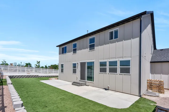 Expansive backyard featuring artificial turf, a concrete patio, and a tiered retaining wall