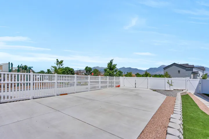 Spacious concrete patio area featuring a privacy fence, artificial turf, decorative gravel, and a terraced retaining wall