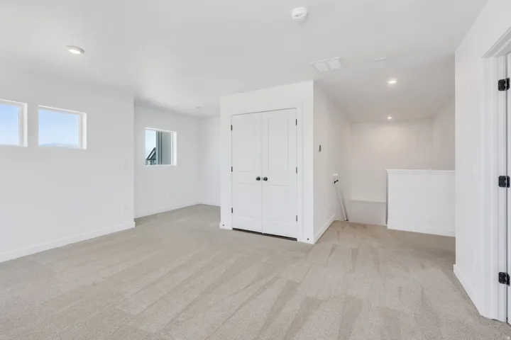 Spacious bonus room featuring light gray carpeting, neutral wall finishes, recessed lighting, and multiple windows