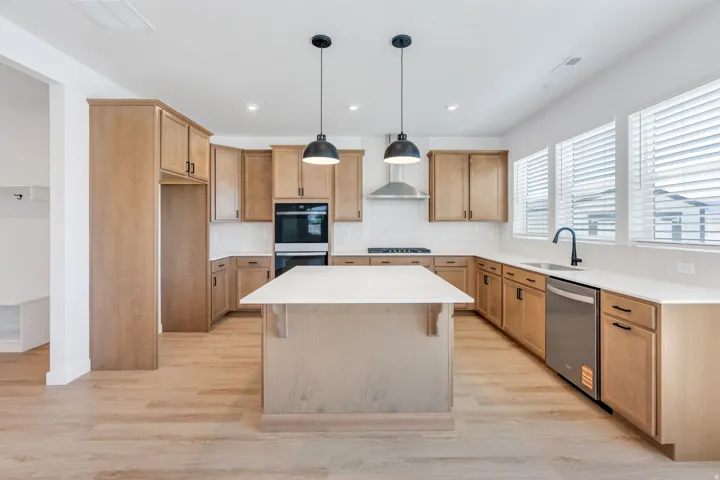 Bright kitchen featuring a central island, light wood-finish cabinetry, stainless steel appliances, a white tile backsplash, and extensive countertop space