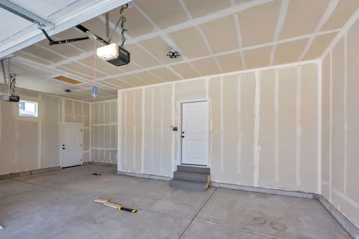 Spacious garage featuring concrete flooring, unpainted drywall, two white interior doors, and a small window