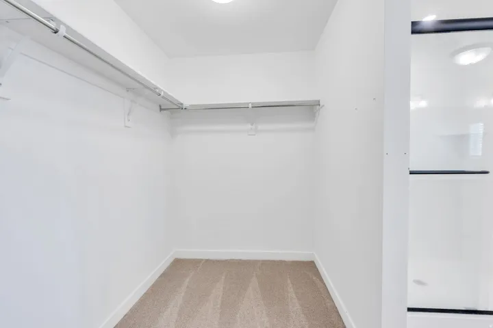 Walk-in closet featuring light-colored carpeting, white baseboards, and multiple hanging rods for organization