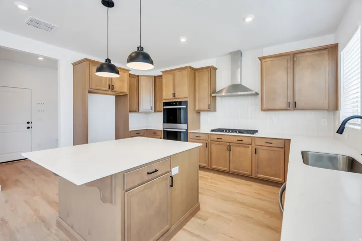 Kitchen featuring light wood cabinetry, white countertops, stainless steel appliances, a center island with pendant lighting, and light wood-finish flooring