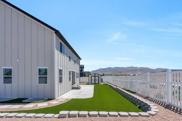 Spacious backyard featuring a concrete patio, artificial turf, and a white picket fence