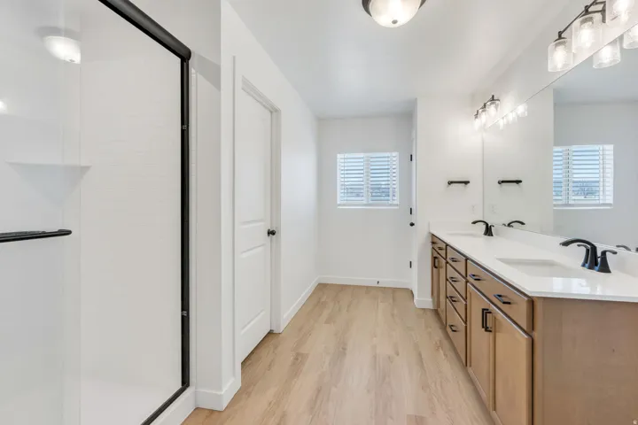 Bathroom featuring a dual vanity with light wood-finish cabinetry, white countertop, and matte black fixtures