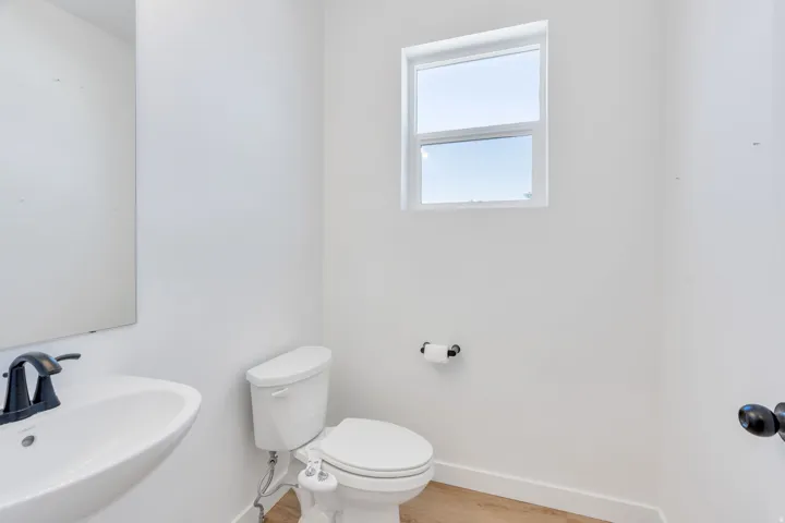 Bathroom featuring a wall-mounted sink with a matte black faucet, a white toilet, wood-finish flooring, and a single window