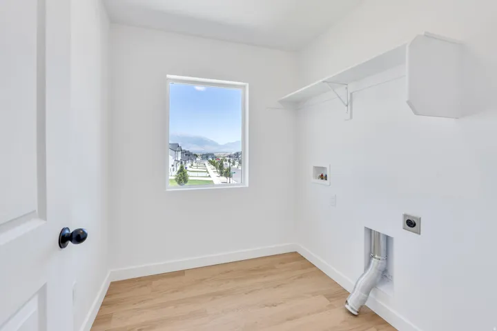 Dedicated laundry space featuring a window, built-in shelving, wood-finish flooring, and white baseboards