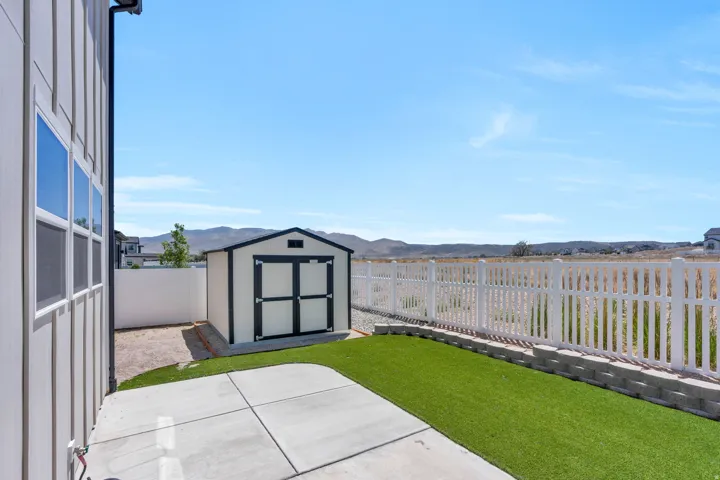 Exterior space featuring a shed, concrete patio, artificial turf, and white picket fencing