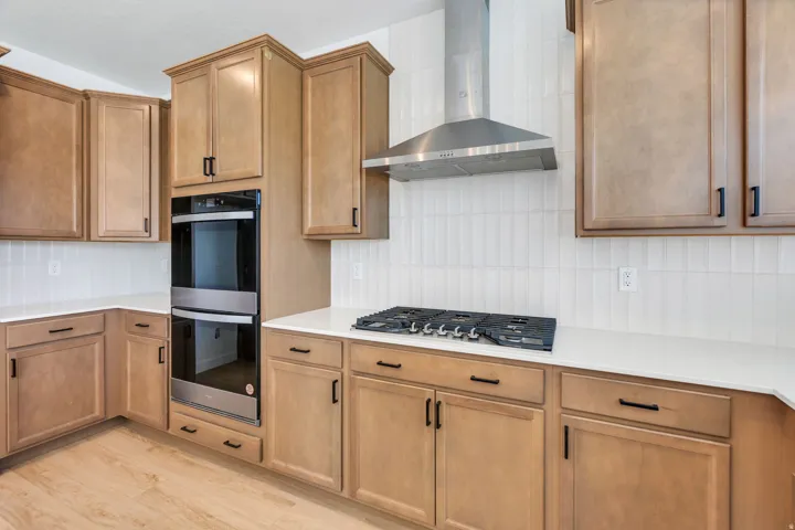Kitchen featuring light wood cabinetry, white countertops, stainless steel wall ovens, a gas cooktop, and a stainless steel range hood