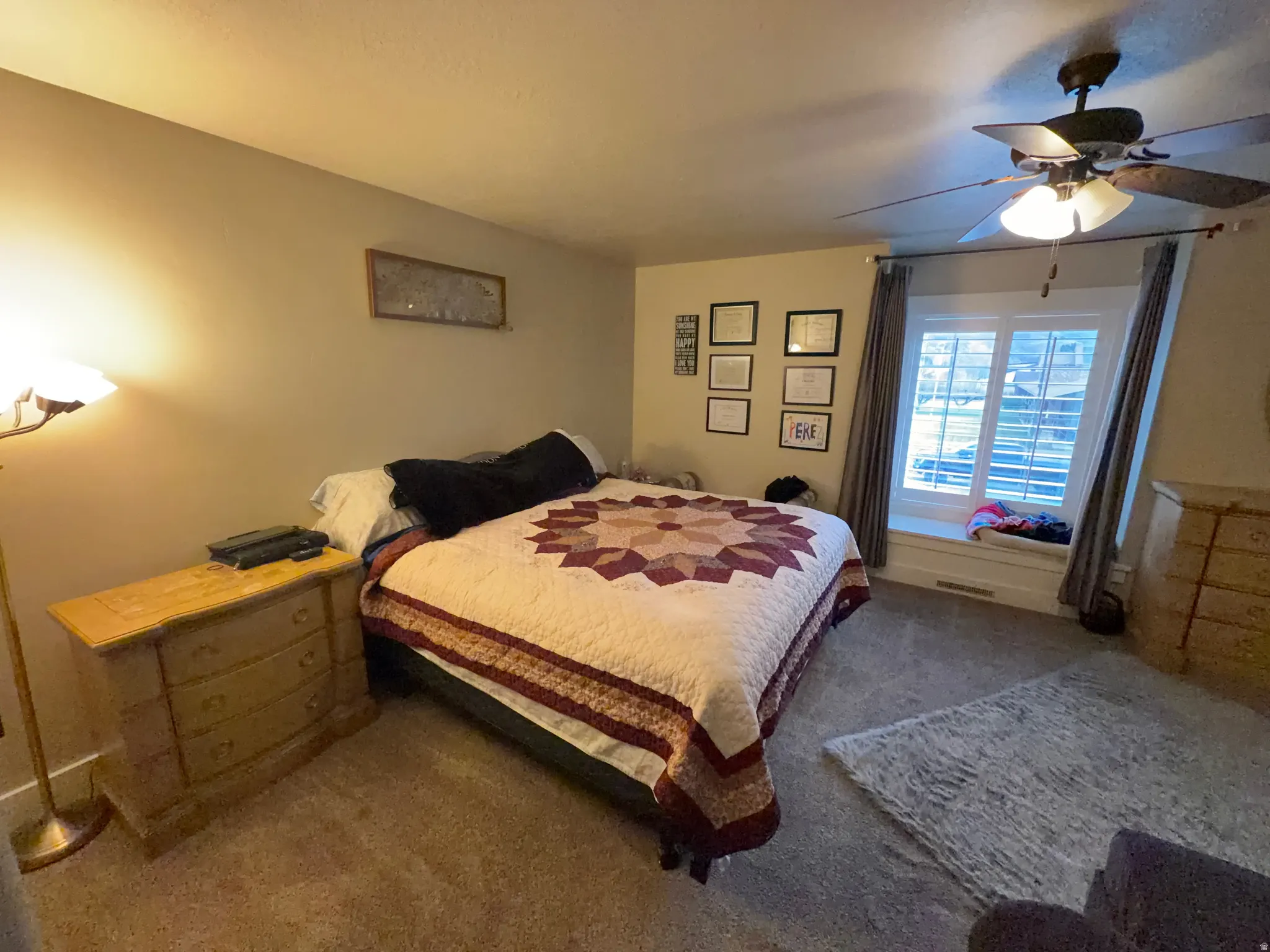 Carpeted room featuring a window with a built-in window seat, ceiling fan with light fixture, and neutral wall tones