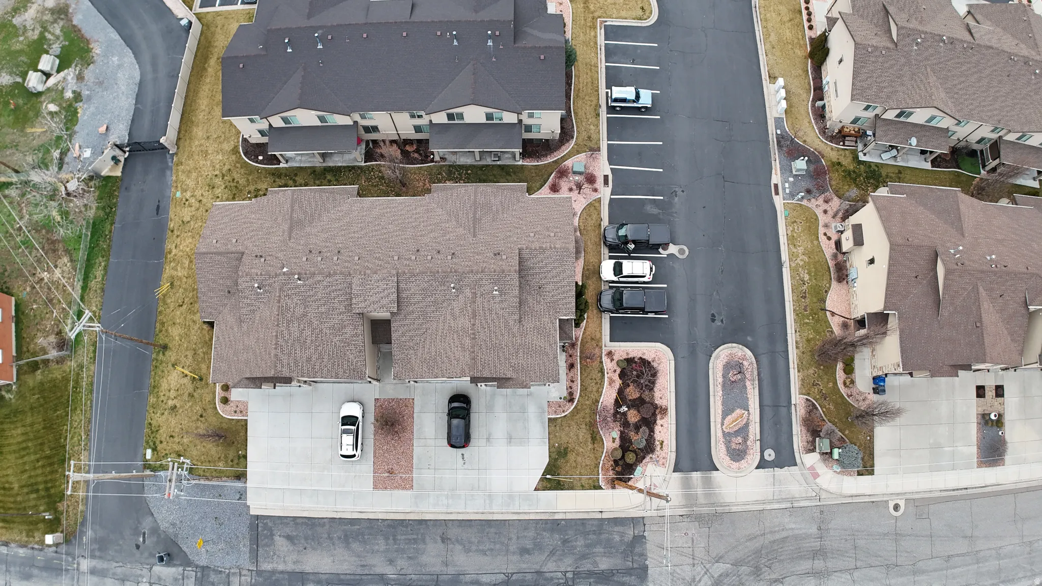 Multi-unit residential property featuring a brown shingle roof, concrete driveway, and landscaped perimeter