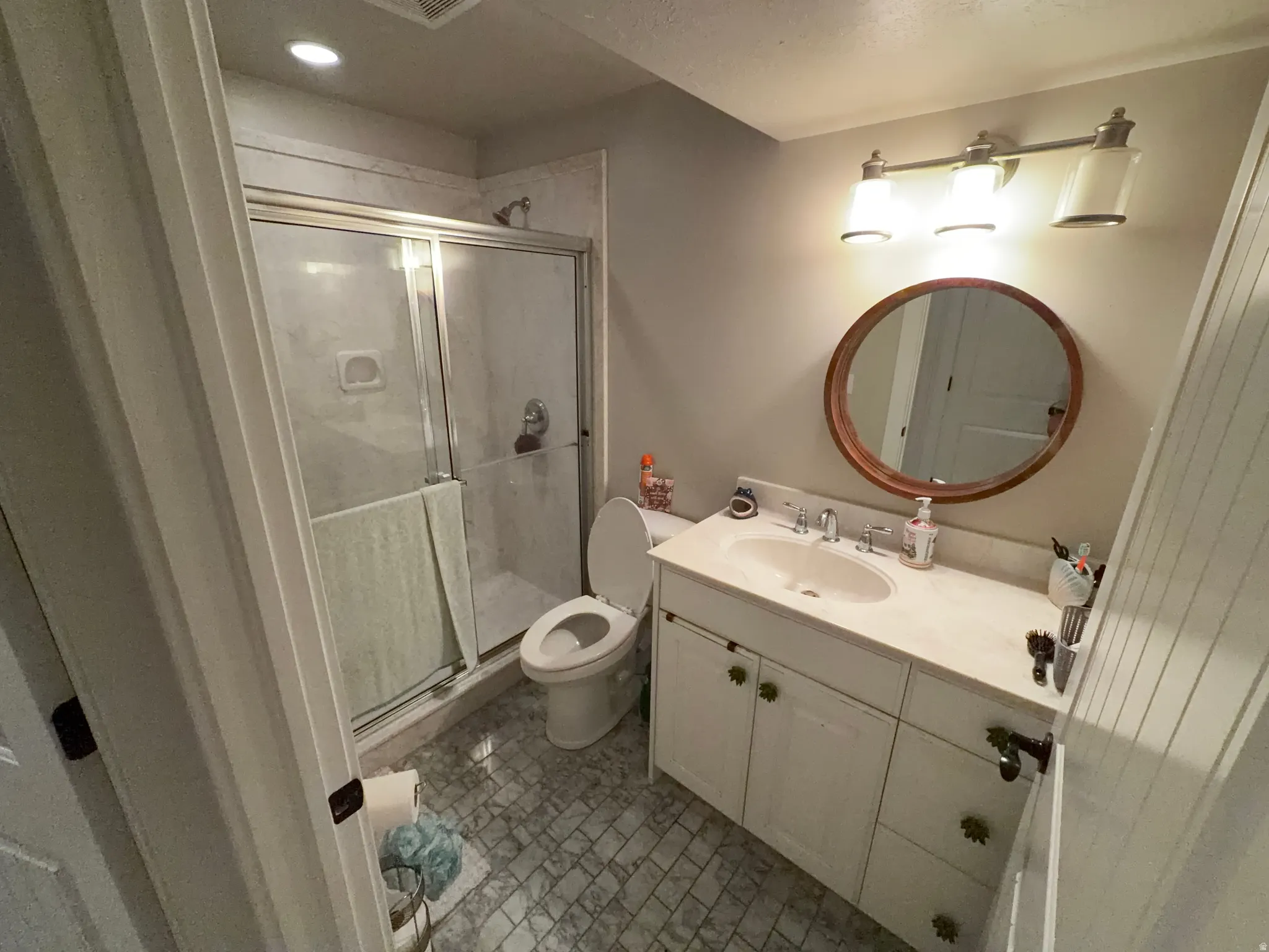Bathroom featuring a glass-enclosed shower, white vanity with an integrated sink, and an overhead vanity light fixture