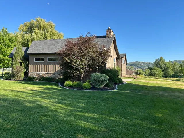 Exterior featuring vertical wood siding, stone facade, a shingled roof, a stone chimney, and a landscaped foundation planting bed