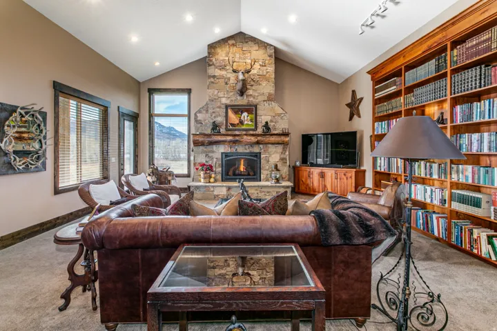 Vaulted ceiling great room featuring a stone fireplace, built-in timber mantel, and an extensive custom wood bookcase