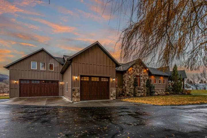 Exterior featuring board and batten siding, stone accents, two attached garages with wood-finish doors, and multiple windows
