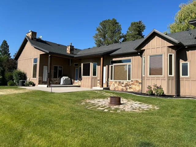 Expansive rear exterior featuring a concrete patio, board and batten siding, stone veneer accents, and multiple windows