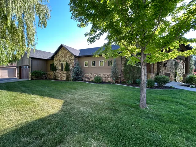 Stone and siding exterior featuring an attached garage with a wood-finish door, a manicured lawn, mature trees, and a paved driveway