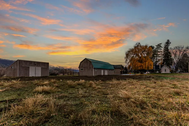 Expansive rural property featuring two outbuildings with metal roofs, a barn-style structure, and a secondary dwelling