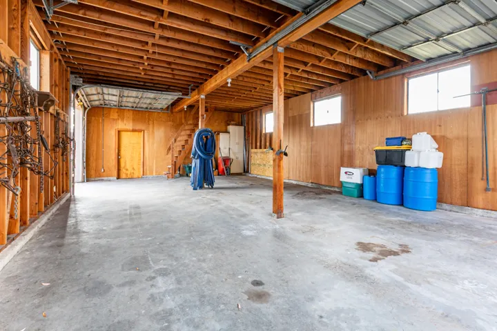 Spacious open garage with concrete flooring, exposed wood beam ceiling, and wood paneling
